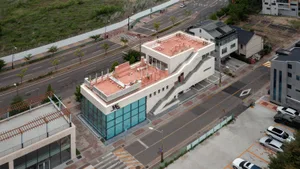A modern building with a red roof and a staircase made of concrete, set against a white background