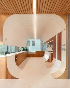Open modern kitchen and dining area with wooden floors and walls, featuring a refrigerator, dining table, chairs, and potted plants