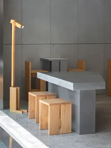 A modern dining space with a large gray concrete table surrounded by wooden stools and four chairs, exuding a minimalist and contemporary atmosphere