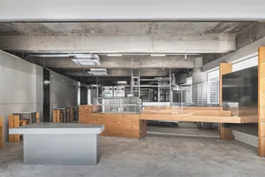 Industrial kitchen with a large wooden countertop, sink, ovens, and refrigerator, giving off a modern and sleek vibe