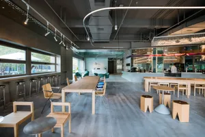 Open modern restaurant interior with a large wooden dining table, grey tile flooring, and potted plants