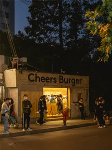A casual restaurant exterior with a brick wall, people waiting outside the entrance, and a welcoming atmosphere