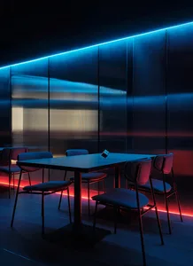A dark and moody dining area with a long wooden table and black chairs, surrounded by dim lighting