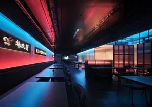 A modern Asian restaurant with a dining area featuring multiple tables and chairs, wood, glass, and metal elements, and an inviting atmosphere
