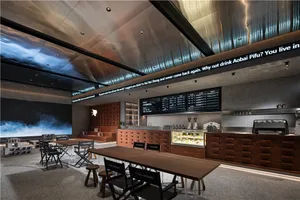 Cozy restaurant interior with wooden floors, a bar, and chairs with black seats, surrounded by tables and beverage cups