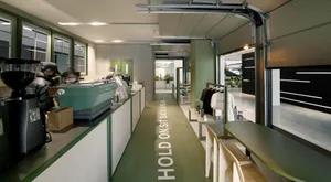 A cozy cafe interior with a green floor, walls, and potted plants, featuring chairs and a welcoming atmosphere