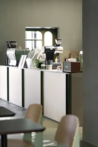 A modern coffee shop with green walls, multiple seating areas, and dining tables, creating a welcoming atmosphere