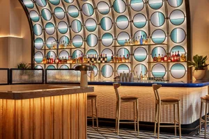 A modern bar with a long wooden counter and stools, featuring bottles and an inviting atmosphere