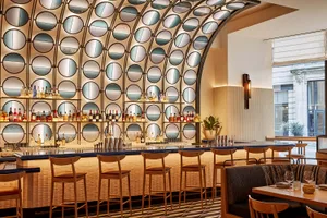 A modern bar area with a long counter and multiple chairs, featuring bottles and a sophisticated atmosphere