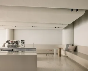 Empty commercial kitchen with white walls and floors, featuring two couches, a dining table, and scattered cups and bottles