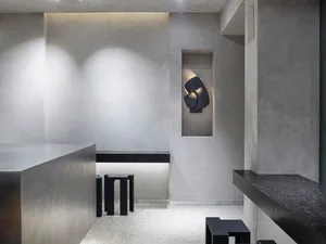 Empty minimalist room with a concrete wall, black countertop, and a dining table, featuring two chairs and a functional atmosphere