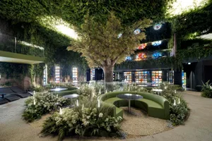 A spacious interior space with a large tree, multiple chairs, and dining tables, surrounded by benches and greenery