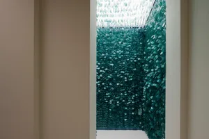 Modern bathroom with a large glass wall featuring green glass pieces and small windows, allowing natural light to enter the space