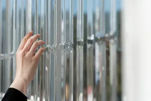 A hand reaches through a glass wall in a minimalist space with clear glass panels and no other objects or people