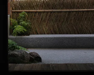 A serene outdoor patio area with a wooden bench and bamboo fence, surrounded by potted plants and greenery