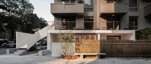 A modern building with multiple balconies and staircases, featuring outdoor seating areas, potted plants, and trees, with neutral tones and a calm atmosphere