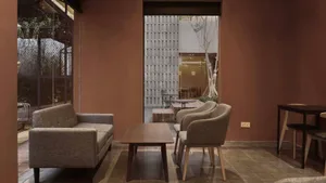Cozy living space with two couches, three chairs, a dining table, and wooden furniture in a warm brown color scheme, filled with natural light