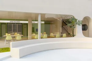 A modern restaurant with comfortable seating areas, natural light, and potted plants, featuring various chairs and benches around dining tables