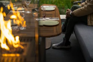 A person sits at a wooden table in an outdoor dining area surrounded by chairs, wine glasses, cups, and bowls, in a relaxed and inviting atmosphere