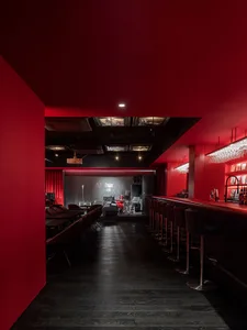 Inviting bar area with a long counter, stools, chairs, and wine glasses, set against a red-themed backdrop