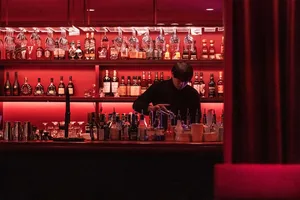 A cozy bar area with a long wooden counter featuring bottles of liquor, wine glasses, cups, and bowls, set in a warm and inviting atmosphere