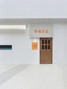 A traditional Asian building with a wooden door featuring Chinese writing, leading to a small room with a sign above it, set against a brick backdrop
