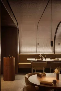 A modern restaurant with a dining area featuring wooden furniture, chairs, and a large table, with bottles scattered throughout, creating an inviting and comfortable atmosphere