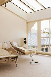 A modern living area with two couches, a chair, and a book, surrounded by natural light from a large window