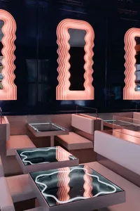 A well-lit restaurant space with multiple seating areas, glass-topped tables, and black and white walls, creating a stylish atmosphere