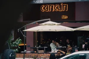 Outdoor dining area with tables, chairs, umbrellas, and potted plants, featuring patrons enjoying their meals in a relaxed atmosphere