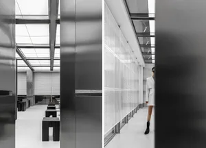 A modern dining space with wooden tables and metal chairs, featuring a woman walking through the room, with a bright and airy atmosphere due to natural light