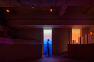 A person walks down a hallway with a concrete floor, creating a sense of depth and atmosphere