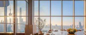 Modern dining area with chairs around a table, wine glasses, and a large window offering a city skyline view
