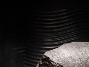 A dark and moody interior space with a large rock at its center, surrounded by black walls and no other objects or people