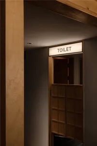 A simple bathroom entrance with a wooden frame and a white sign reading 'Toilet' above it, leading to a small, darkened space