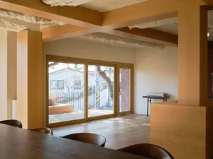Warm and inviting open concept living area with wooden floors and walls, featuring a dining table, chairs, and a potted plant