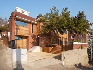 A charming house with a red brick exterior, surrounded by trees and a parked car, set against a natural background