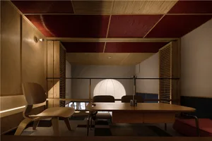 Dining area with a wooden table, two chairs, a couch, and red accent walls, set in a modern space with clean lines and minimal decoration