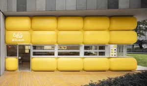 A modern building with large, round, yellow pillars made of a wood-plastic material, featuring multiple windows and seating areas