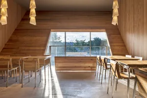 Open restaurant interior with wooden floors and walls, multiple dining tables, and natural light from windows