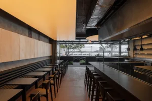 A modern restaurant interior with a large dining area, potted plants, and comfortable seating