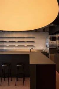 Industrial kitchen with a black countertop, stools, a refrigerator, and an oven, with a modern and functional atmosphere