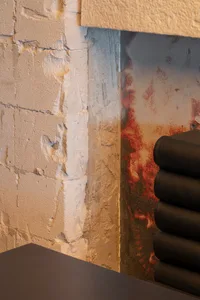 A darkened interior wall with a red stain and two black leather chairs, one on either side of the wall