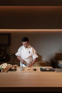 A man prepares food in a warm and inviting Asian-style kitchen with a wooden countertop, various kitchen items, and bottles