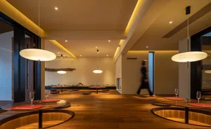 Empty restaurant with wooden floors and walls, featuring dining tables and a person walking through the space, creating a calm and inviting atmosphere