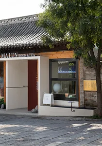 Asian-style house with a red door and a white wall, surrounded by two trees and a window with a sign