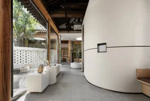 Open living area with a large white wall, decorative vases, a bookshelf, and natural light from windows