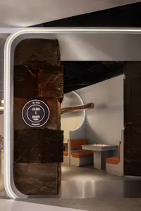 Cozy cafe interior with a stone wall, wooden elements, and two orange chairs in a dimly lit space