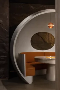 A modern restaurant dining area with a circular wooden table and two chairs, surrounded by clean lines and minimalistic decoration, creating a cozy ambiance