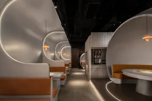 A dimly lit restaurant with a long hallway lined with tables and chairs, featuring a mix of wood and metal materials and focused lighting on the dining tables
